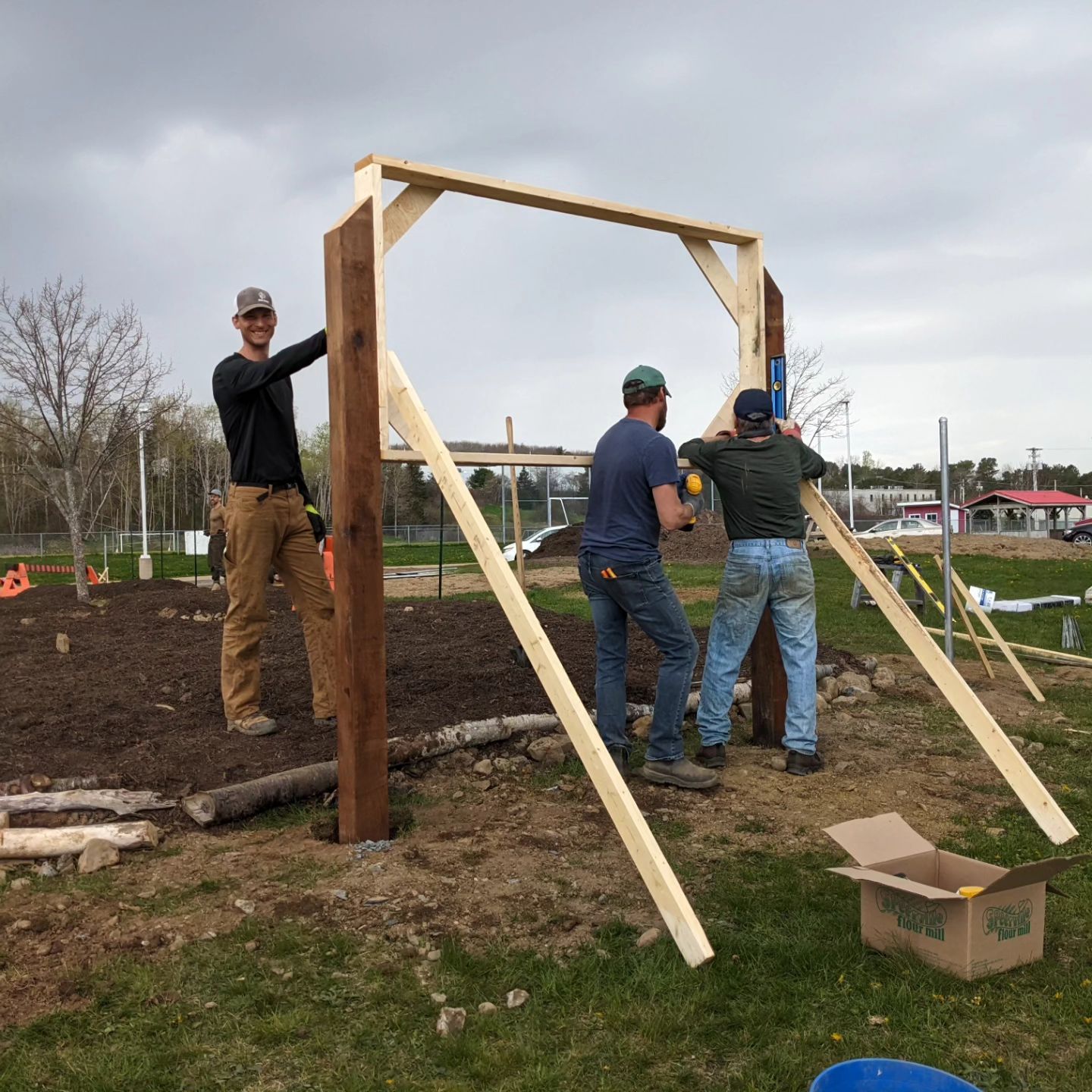 Three people work on the wood frame of an outdoor bulletin board.